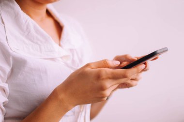 Beyaz arka planda akıllı telefon tutan genç bir kadının yakın plan görüntüsü.