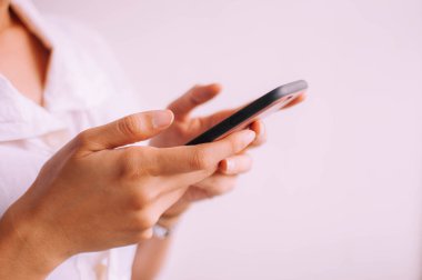 Beyaz arka planda akıllı telefon tutan genç bir kadının yakın plan görüntüsü.