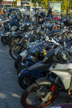 Motosikletlerin ön tekerleri bir otoparkta açıkta. Birçok park edilmiş motosiklet. 