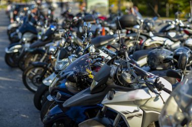 Motosikletlerin ön tekerleri bir otoparkta açıkta. Birçok park edilmiş motosiklet. 