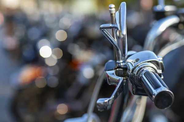 The chromed handlebar of a motorcycle.  View of motorcycle handlebar in the background many motorbikes blurred.