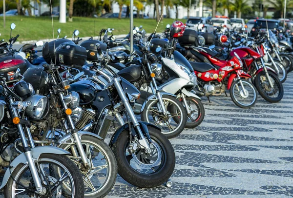 Motosikletlerin ön tekerleri bir otoparkta açıkta. Birçok park edilmiş motosiklet. 