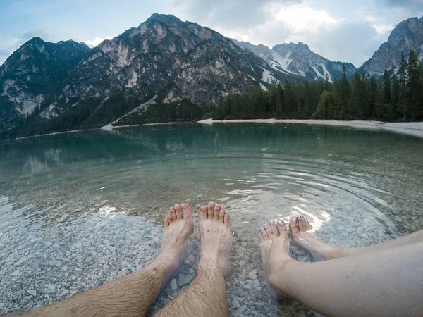 Mans and womens leg against amazing view of Braies Lake Lago with forest and mountains reflected in lake water Dolomites Alps, Italy. Captured on Gopro hero 5 hero5. Hiking travel and adventure.