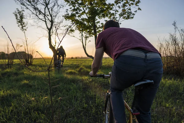 Man fietsen in de zonsondergang. Fietsen bij zonsondergang. Gezonde levensstijl Concept. Mannelijke rit fiets in de zonsondergang. Biker fietsen op zonsondergang hemel op een veld. Sport. — Stockfoto