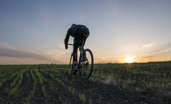 Lutsk, Ukraine - April 5, 2018: Man rides a bicycle in sunset on a field. — Stock Photo, Image