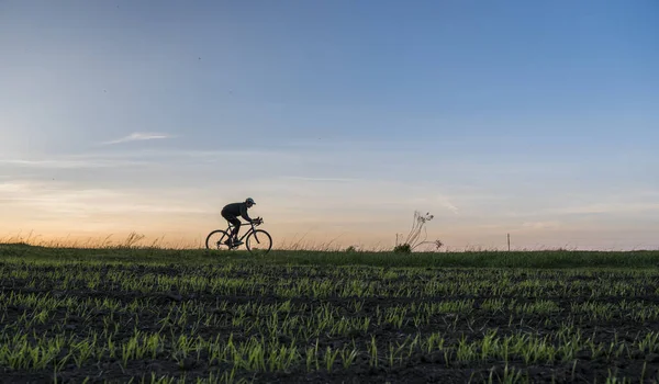 Lutsk, Oekraïne - 5 April 2018: Man rijdt een fiets in de zonsondergang op een veld. — Stockfoto