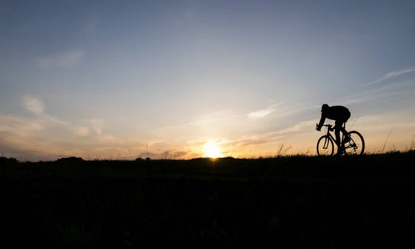 Lutsk, ukraine - 5. April 2018: Mann fährt Fahrrad bei Sonnenuntergang auf einem Feld. — Stockfoto