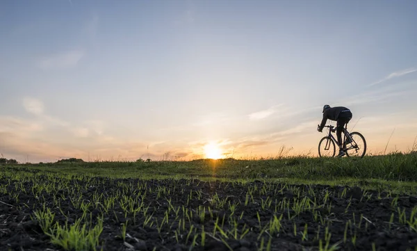 Lutsk, Oekraïne - 5 April 2018: Man rijdt een fiets in de zonsondergang op een veld. — Stockfoto