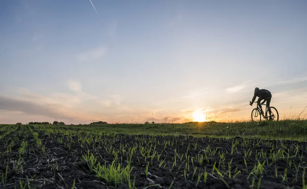 Lutsk, Ucrânia - 5 de abril de 2018: Homem anda de bicicleta ao pôr-do-sol em um campo . — Fotografia de Stock