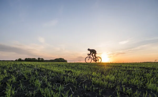 Lutsk, Ucrânia - 5 de abril de 2018: Homem anda de bicicleta ao pôr-do-sol em um campo . — Fotografia de Stock