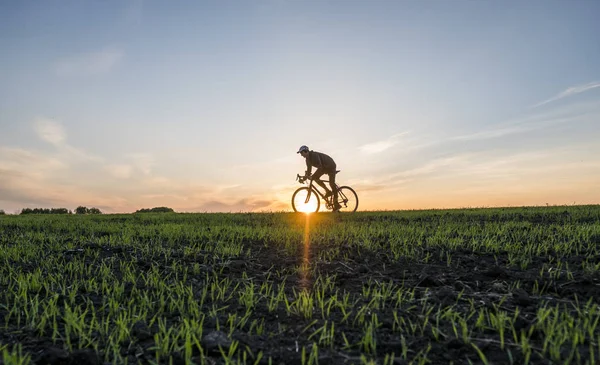 Lutsk, Ucrania - 5 de abril de 2018: El hombre monta una bicicleta al atardecer en un campo . — Foto de Stock