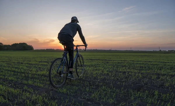 Lutsk, Oekraïne - 5 April 2018: Man rijdt een fiets in de zonsondergang op een veld. — Stockfoto
