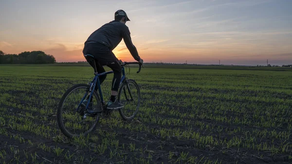 Lutsk, Ukraine - April 5, 2018: Man rides a bicycle in sunset on a field. — Stock Photo, Image