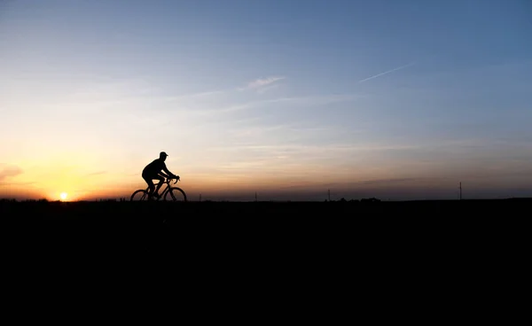 Lutsk, Ucrânia - 5 de abril de 2018: Homem anda de bicicleta ao pôr-do-sol em um campo . — Fotografia de Stock