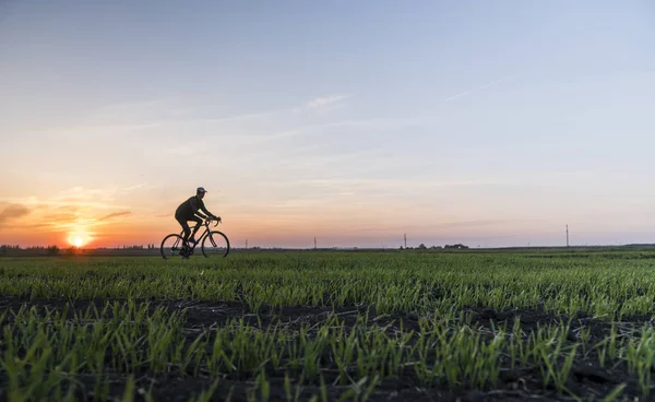 Lutsk, Oekraïne - 5 April 2018: Man rijdt een fiets in de zonsondergang op een veld. — Stockfoto