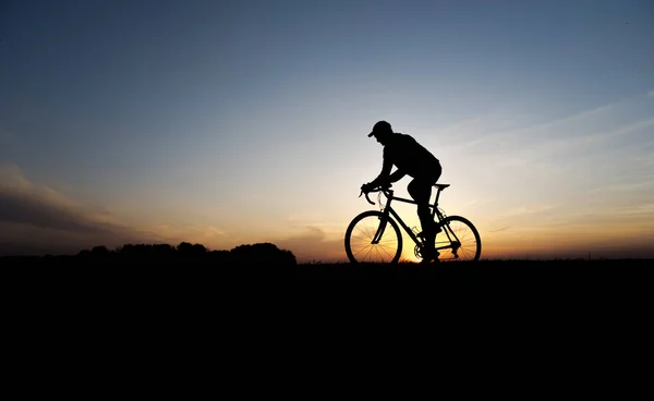 Lutsk, ukraine - 5. April 2018: Mann fährt Fahrrad bei Sonnenuntergang auf einem Feld. — Stockfoto
