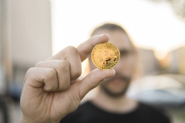 Elinde bir adam bir bulanık günbatımı zemin üzerine altın Bitcoin madeni para. Bir kripto para birimi sanal para tutan el. İş, ticaret, Döviz, dijital para.