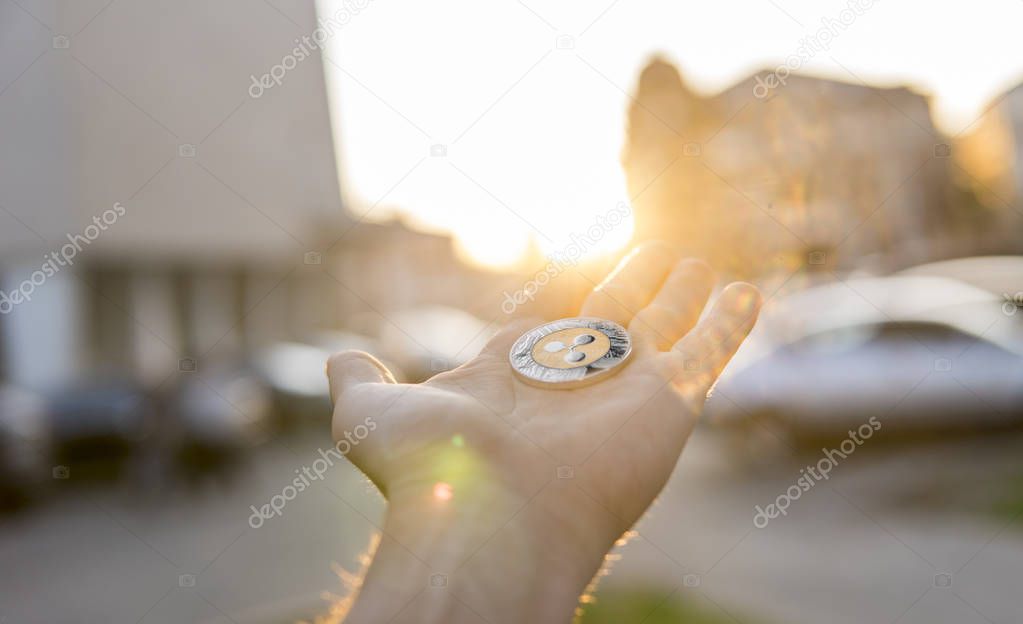 Golden silver Ripple coin in hand on a blurred sunset background. Hand holding a crypto currency virtual money. Bussiness, commercial, exchange, digital money.