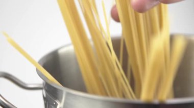 Beyaz bir arka plan üzerinde çelik bir tavada spagetti aşağı bir aşçı koyar.