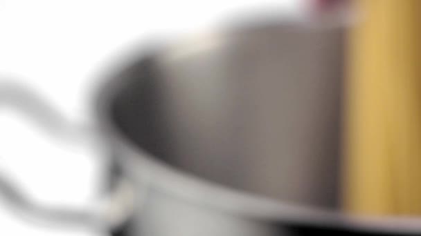 Ένας μάγειρας που βάζει κάτω ένα σπαγγέτι σε μια κατσαρόλα με χάλυβα σε λευκό φόντο. — Αρχείο Βίντεο