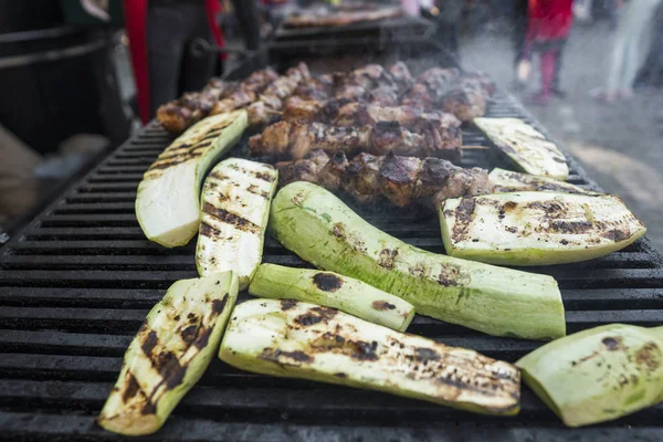 Zucchini and meat shish cooking on a grill.