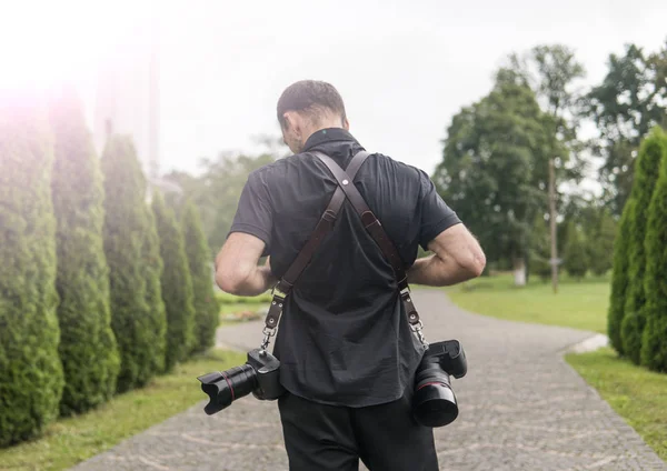 Costas de fotógrafo de casamento profissional em camisa preta e com duas câmeras e um ombro tiras contra o jardim verde. Fotografia casamento . — Fotografia de Stock