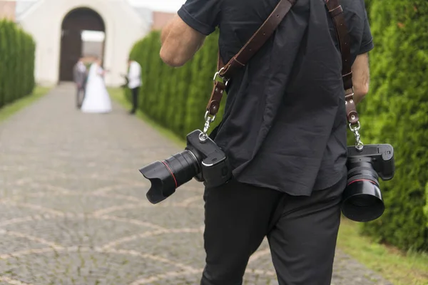 Fotograf ślubny profesjonalne robi zdjęcia panny młodej i pana młodego w ogrodzie, fotograf w akcji z dwóch kamer na ramiączka. — Zdjęcie stockowe