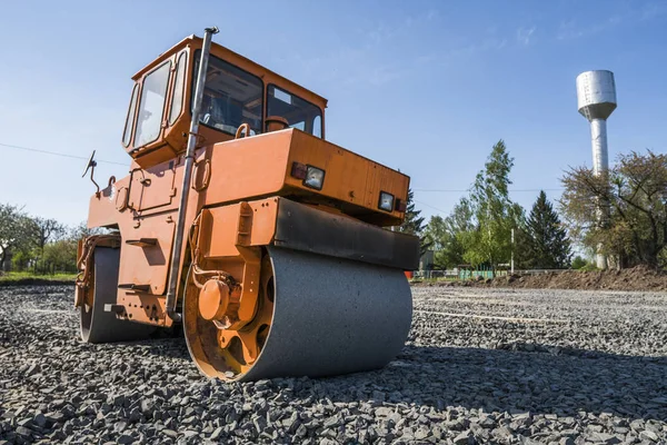 Orange light Vibration roller compactor standing on a stones at road construction and repairing asphalt pavement works with a blue sky. — Stock Photo, Image