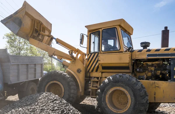 Carregador amarelo entregando cascalho de pedra em caminhão durante obras de construção de estradas. As pedras para a estrada. Pedra de descarga . — Fotografia de Stock