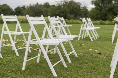 Beyaz düğün sandalye yeşil çimenlerin üzerinde taze çiçekler ile dekore edilmiştir. Konuklar bahçede düğün töreni için hazırlanan yeşil çim üzerinde için boş ahşap sandalye.