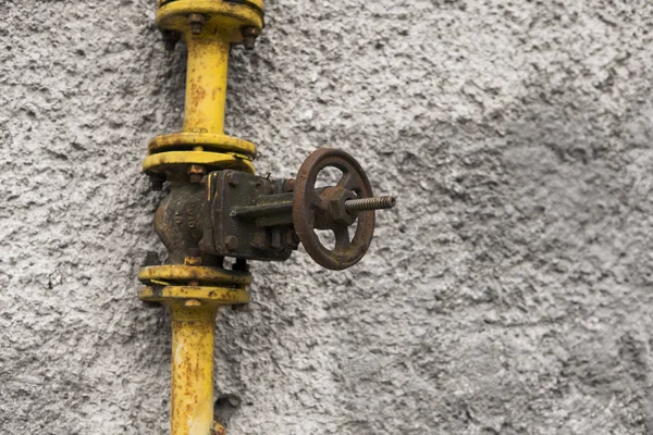 Old weathered gas crane and pipe on the background of a gray wall. Old gas gate of yellow colour is on a pipe and blocks a pipe. The pipeline with cranes for gas giving on the wall. — Stock Photo, Image