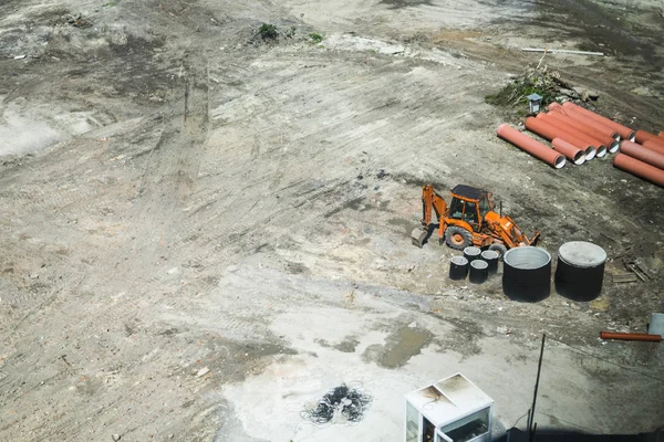 Oranžový bagr, stojící na pozemku během výstavby nové budovy v oblasti města. Letecký pohled na stavebnictví stavební místo. Stavební stroje. — Stock fotografie