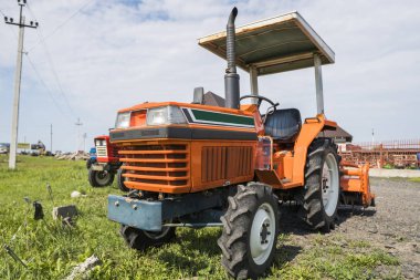 Küçük mini turuncu Traktör çiftlik yarda yeşil çimenlerin üzerinde duruyor ve işe başlamak bekler.