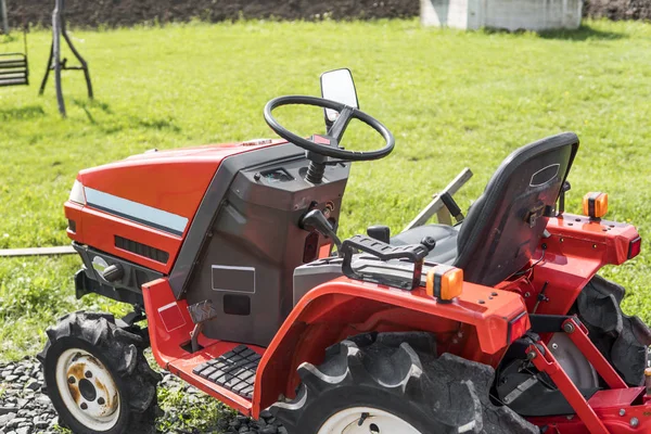 Małe mini traktor czerwony stoi na farmie na zielonej trawie i czeka na pracy, aby rozpocząć. — Zdjęcie stockowe