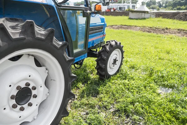 A small mini blue tractor stands on a farm yard on green grass and waits for work to begin.