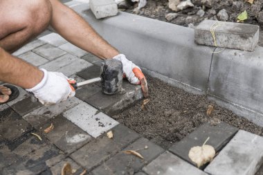 Onun turuncu bir üreticisi eller eller dikkatle yerleştirerek bir pozisyonda düzeltilmiş ve komisyonlu topraklarında temel yeni dış parke taşı döşeme uydurma bir çekiçle eldivenli. Kum Vakfı. Bina.