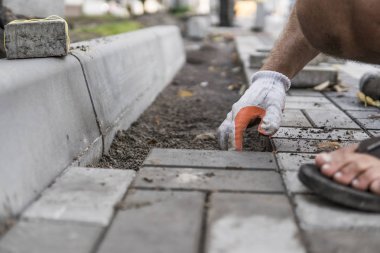 Onun turuncu bir üreticisi eller eller dikkatle yerleştirerek bir pozisyonda düzeltilmiş ve komisyonlu topraklarında temel yeni dış parke taşı döşeme uydurma bir çekiçle eldivenli. Kum Vakfı. Bina.