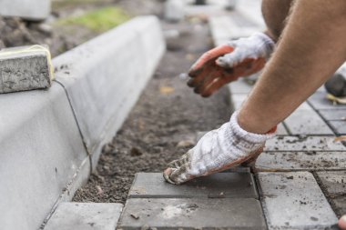 Onun turuncu bir üreticisi eller eller dikkatle yerleştirerek bir pozisyonda düzeltilmiş ve komisyonlu topraklarında temel yeni dış parke taşı döşeme uydurma bir çekiçle eldivenli. Kum Vakfı. Bina.