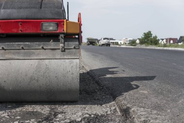 Turuncu titreşim silindir kompaktör ayakta asphalts yol yol yapım ve tamir asfalt kaplama yakınındaki bir zeminde mavi gökyüzü ile çalışır.