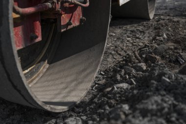 Turuncu titreşim silindir kompaktör ayakta asphalts yol yol yapım ve tamir asfalt kaplama yakınındaki bir zeminde mavi gökyüzü ile çalışır.