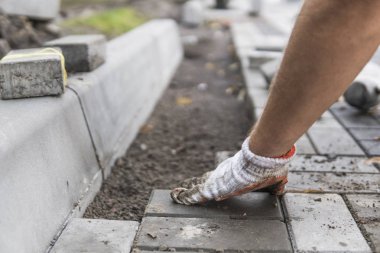Onun turuncu bir üreticisi eller eller dikkatle yerleştirerek bir pozisyonda düzeltilmiş ve komisyonlu topraklarında temel yeni dış parke taşı döşeme uydurma bir çekiçle eldivenli. Kum Vakfı. Bina.