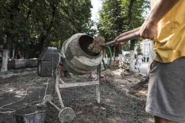 İnşaat işçisi kürek kaldırım inşaatı sırasında kullanarak site oluşturma, beton karıştırıcı karıştırma için malzemeyi ekleyin.