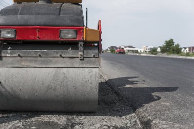 Turuncu titreşim silindir kompaktör ayakta asphalts yol yol yapım ve tamir asfalt kaplama yakınındaki bir zeminde mavi gökyüzü ile çalışır.