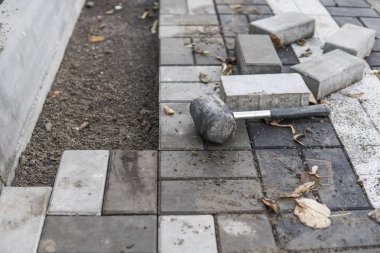 Onun turuncu bir üreticisi eller eller dikkatle yerleştirerek bir pozisyonda düzeltilmiş ve komisyonlu topraklarında temel yeni dış parke taşı döşeme uydurma bir çekiçle eldivenli. Kum Vakfı. Bina.