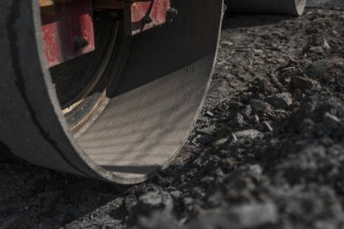 Turuncu titreşim silindir kompaktör ayakta asphalts yol yol yapım ve tamir asfalt kaplama yakınındaki bir zeminde mavi gökyüzü ile çalışır.