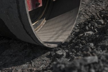 Turuncu titreşim silindir kompaktör ayakta asphalts yol yol yapım ve tamir asfalt kaplama yakınındaki bir zeminde mavi gökyüzü ile çalışır.