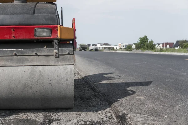 Turuncu titreşim silindir kompaktör ayakta asphalts yol yol yapım ve tamir asfalt kaplama yakınındaki bir zeminde mavi gökyüzü ile çalışır.