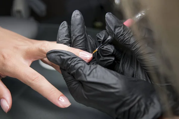 Маникюрша делает педикюрную процедуру восстановления и наращивания ногтей на ногтях девушки в маникюрном салоне. Крупный план женщины руки в маникюре, получающей маникюр от косметолога . — стоковое фото