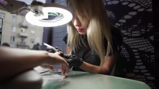 The manicurist makes pedicure procedure of recovery and nail extensions on the nails of the girl in the nail salon . Closeup shot of a woman hands in nail salon receiving a manicure by a beautician. — Stock Video