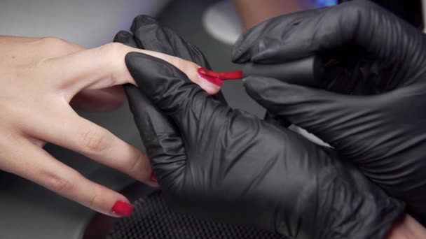 Donna che ha una manicure in un salone di bellezza con una vista da vicino di un'estetista che applica vernice con un applicatore. Master unghie dipinte con smalto. Dettagli colpo di mani applicando chiodo rosso . — Video Stock